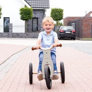 Barn kører på Pinolino Oskar 2-i-1 trehjulet cykel i grå/natur på en flisebelagt vej.