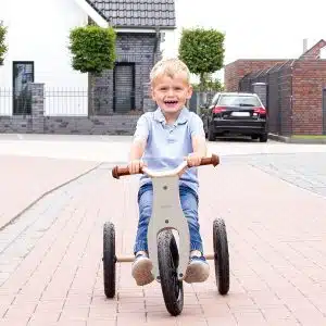 Barn kører på Pinolino Oskar 2-i-1 trehjulet cykel i grå/natur på en flisebelagt vej.