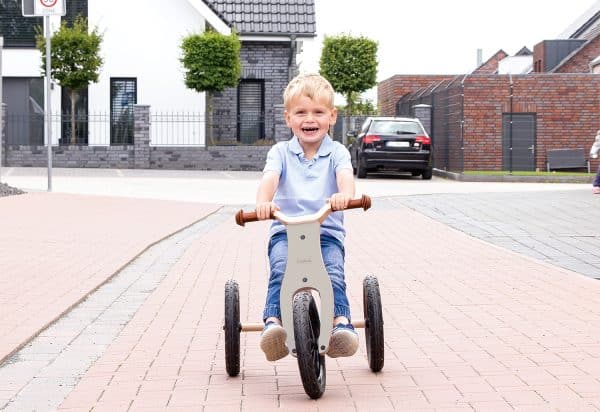 Barn kører på Pinolino Oskar 2-i-1 trehjulet cykel i grå/natur på en flisebelagt vej.