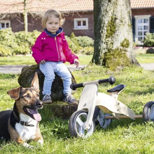 Pinolino Charlie løbecykel i naturtræ med tre hjul i haven ved et barn og en hund