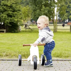 Barn skubber en hvid Pinolino Charlie trehjulet løbecykel på en sti i haven.