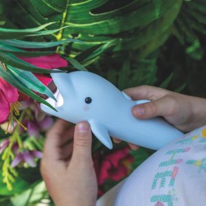 Rabbit & Friends lommelygte Delfinen Bubbly holdt i barnets hænder ved grønne planter